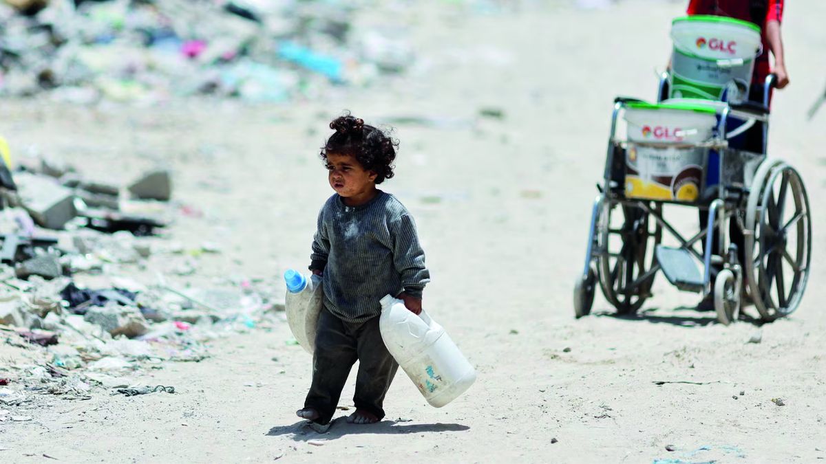 Una niñapalestina lleva latas para recoger agua mientras camina junto a casas quefueron destruidas en un ataque israelí