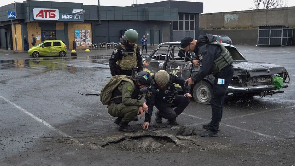 Ucrania: Investigadores policiales inspeccionan un cráter de proyectildejado por un ataque militar ruso en el estacionamiento de un supermercadoubicado en Kherson